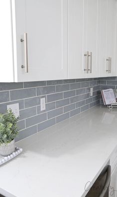 a kitchen with white cabinets and gray tile on the backsplash, countertop