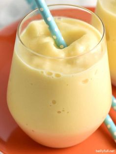 two glasses filled with yellow liquid on top of an orange plate next to blue and white straws