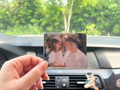 a person holding up a photo in front of a car with an air freshener attached to it