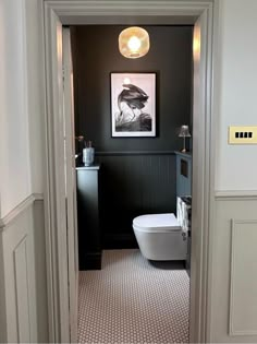 a white toilet sitting in a bathroom next to a black and white wall with a painting on it