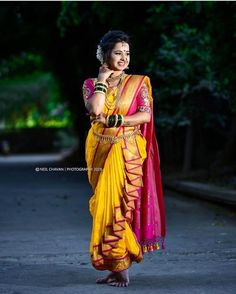 a woman in yellow and pink sari standing on the street with her arms crossed