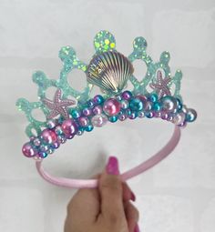 a hand is holding a tiara with pearls and seashells on it's head