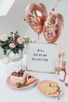 a table topped with cakes and balloons next to a sign that says will you be my valentine?