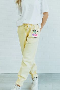 a woman in white shirt and yellow sweatpants standing with her hand on her hip