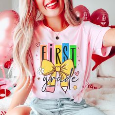 a woman with blonde hair wearing a pink t - shirt that says first grade on it