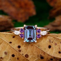 a ring with an amethorate and three diamonds on it sitting on top of a leaf