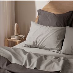 a bed with grey sheets and pillows in a bedroom