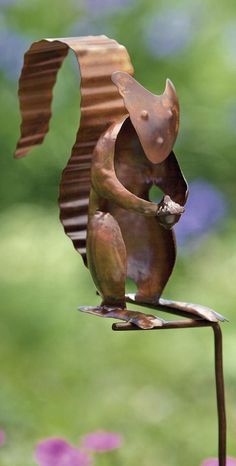 a metal sculpture of a squirrel on top of a piece of wood in the shape of a bird