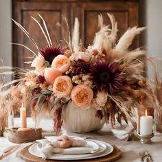 an arrangement of flowers in a white vase on a table with candles and napkins