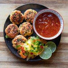 a black plate topped with crab cakes next to a bowl of salsa and lime wedges