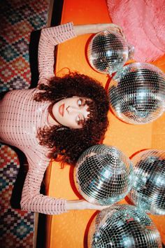 a woman with curly hair is posing in front of disco balls on an orange table