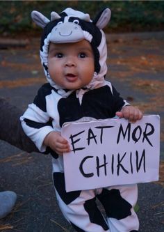 a baby dressed in a cow costume holding a sign that says eat mor chikin