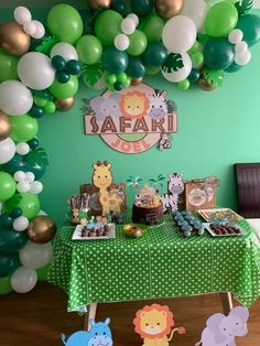 a green table topped with lots of balloons and jungle themed desserts on top of it