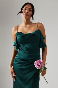 a woman in a green dress holding a pink rose and looking at the camera with her hand on her hip