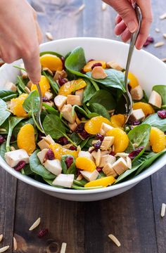 someone cutting into a salad with spinach and oranges