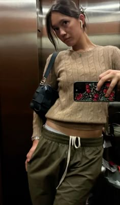 a woman taking a selfie with her cell phone in an elevator stall wearing green sweatpants