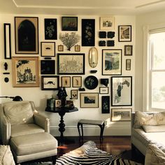 a living room filled with lots of framed pictures on the wall above a couch and chair