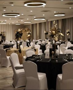 a banquet room with white chairs and black table cloths, gold decorations and lights