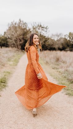 a woman in an orange dress walking down a dirt road