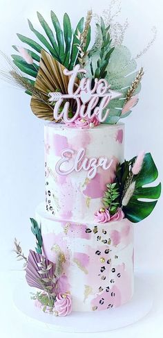 a three tiered cake decorated with pink and green flowers, leaves and acrylic lettering