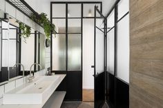 a modern bathroom with black and white fixtures, wood paneling, and a plant hanging over the sink