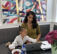 a woman sitting at a table with a child on her lap looking at a laptop