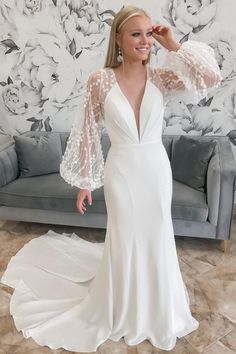 a woman standing in front of a couch wearing a white dress with sheer sleeves and an open back