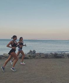 two women running on the beach at sunset or sunrise with water and rocks in the background