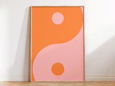 an orange and pink art piece sitting on top of a hard wood floor next to a white wall