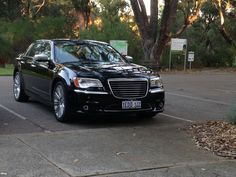 a black car parked in a parking lot next to some trees and bushes on the side of the road