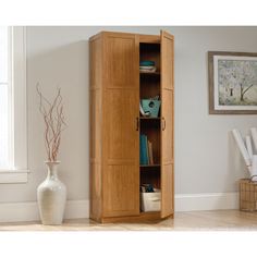 a tall wooden cabinet sitting in a living room next to a vase with flowers on it