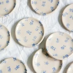 several plates with blue flowers on them sitting on a white tableclothed surface in rows