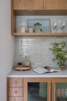 an open book on top of a wooden cabinet next to a vase and wine glasses