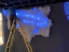 a man standing on a ladder in front of a blue light painting the wall with clouds