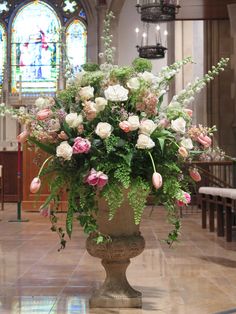 a large vase filled with lots of flowers on top of a floor next to a stained glass window