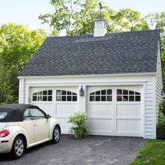 a car parked in front of a white garage with a black roof and shingled windows