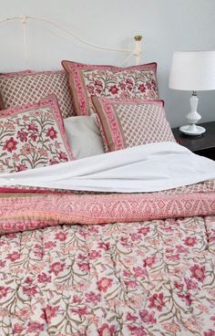 an unmade bed with pink and white floral bedspread