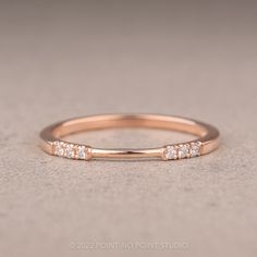 a rose gold wedding band with five diamonds on it, sitting on a gray surface