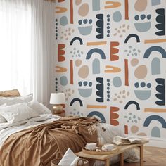 a bed sitting under a window next to a wallpaper covered in colorful shapes and colors