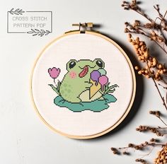 a cross stitch frog sitting on top of a flower