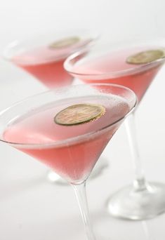 three martini glasses filled with pink liquid and topped with two gold coined pieces on the rim