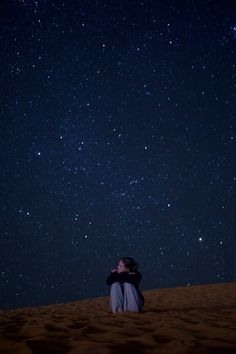 a man sitting on top of a sandy beach under a night sky filled with stars