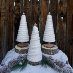 three white knitted christmas trees sitting on top of a wooden table next to pine cones