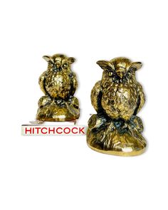 two gold owl figurines sitting on top of each other with the words hitchcock below them