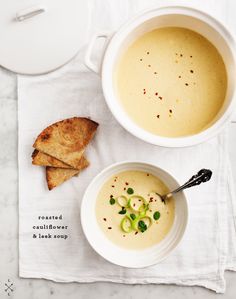 two bowls filled with soup next to bread on top of a white napkin and spoon