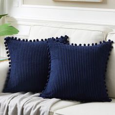 two blue pillows sitting on top of a white couch next to a potted plant