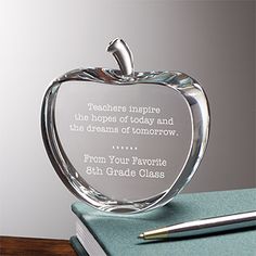 an apple shaped glass award sitting on top of a desk next to a pen and notebook