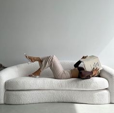 a woman laying on top of a white couch holding a book in her hand and reading