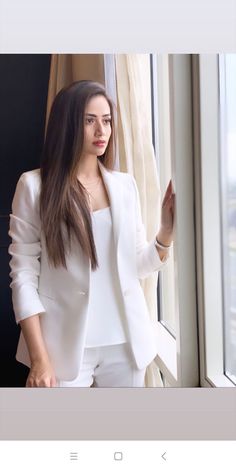 a woman standing next to a window looking out the window