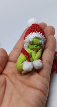 a hand holding a small green and white toy in it's left palm, wearing a santa hat